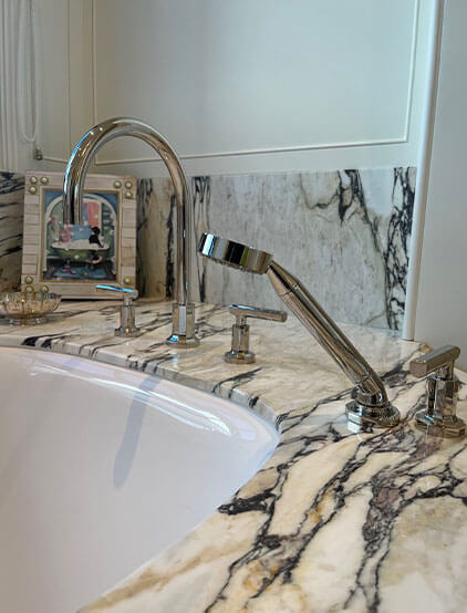 Polished chrome tub filler and hand shower on a marble deck