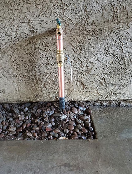 Copper stub-out with a shut-off valve on a stucco wall over a gravel bed